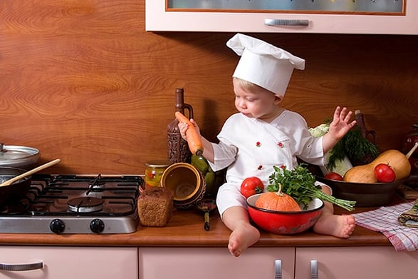 Child sitting on countertop with vegetables in hands
