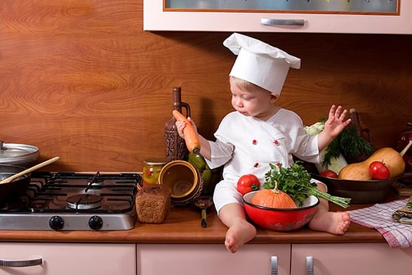 Child sitting on countertop with vegetables in hands 